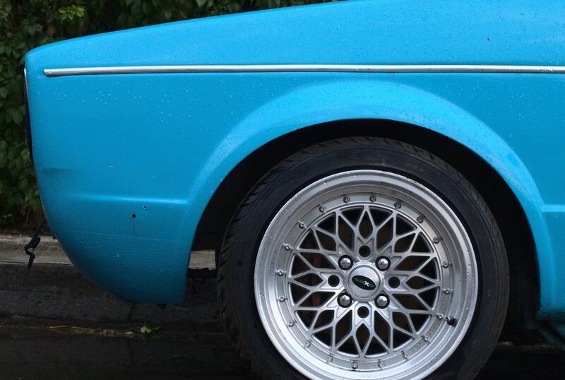 Cerca de un automóvil azul, se observa una llanta con diseño de rayos.